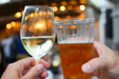 two hands holding up a glass of white wine and a beer