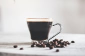 a cup of black coffee with coffee beans scattered around it