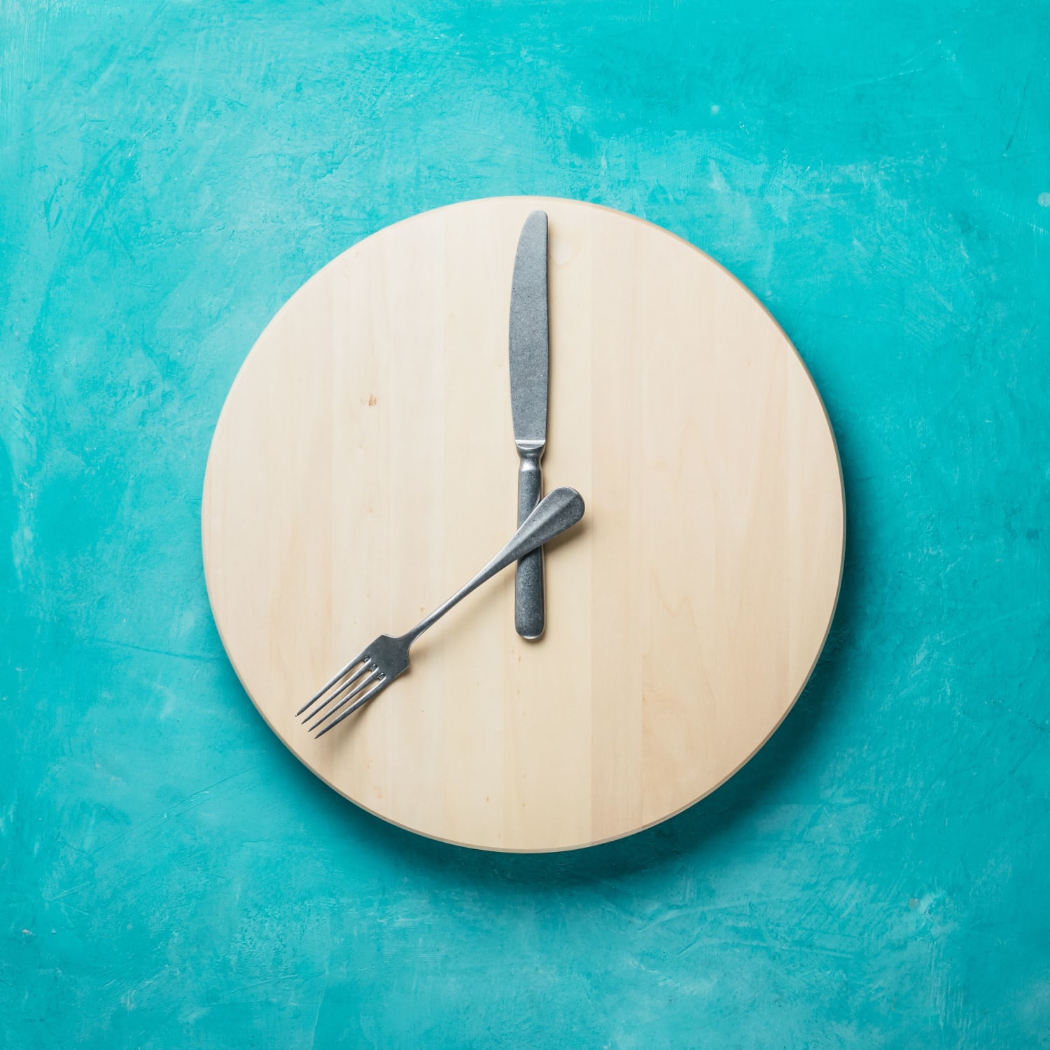 knife and fork on circular chopping board arranged to look like a clock face